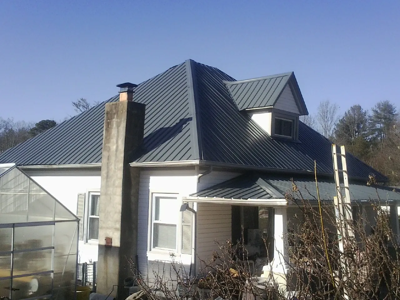 Dark blue standing seam metal roof on a white farmhouse with dormer — Slate & Tile Roof Repair by Roofing Brothers in Saint Clair Shores