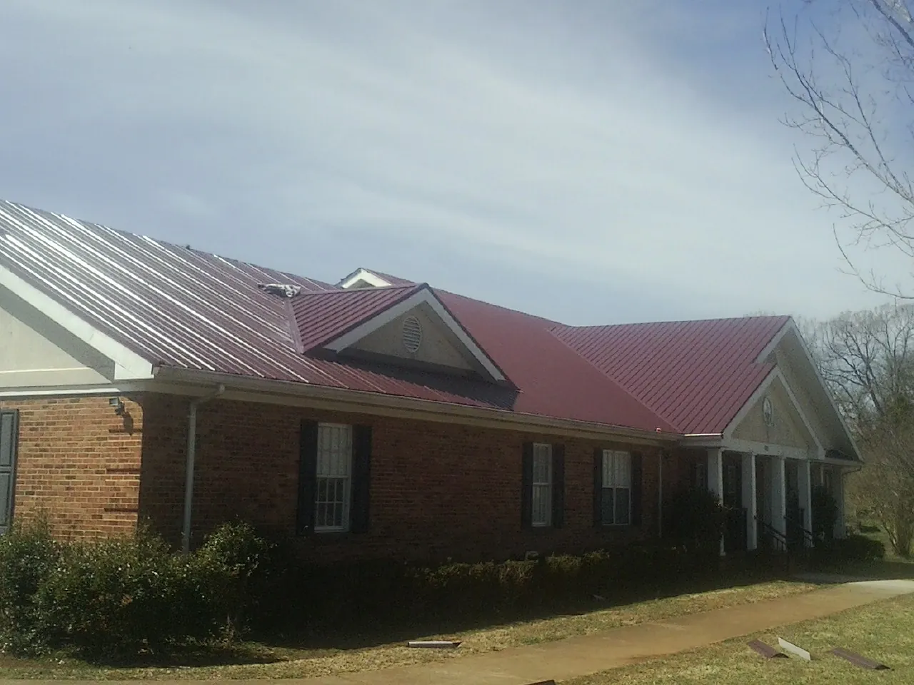 Red metal roof with gabled entries on a long brick building, from a Hail Damage Roof Repair job in Saint Clair Shores