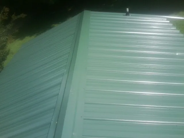 New green metal panels meeting at the ridge of a roof — Flat Roof Repair work by our crew in Saint Clair Shores