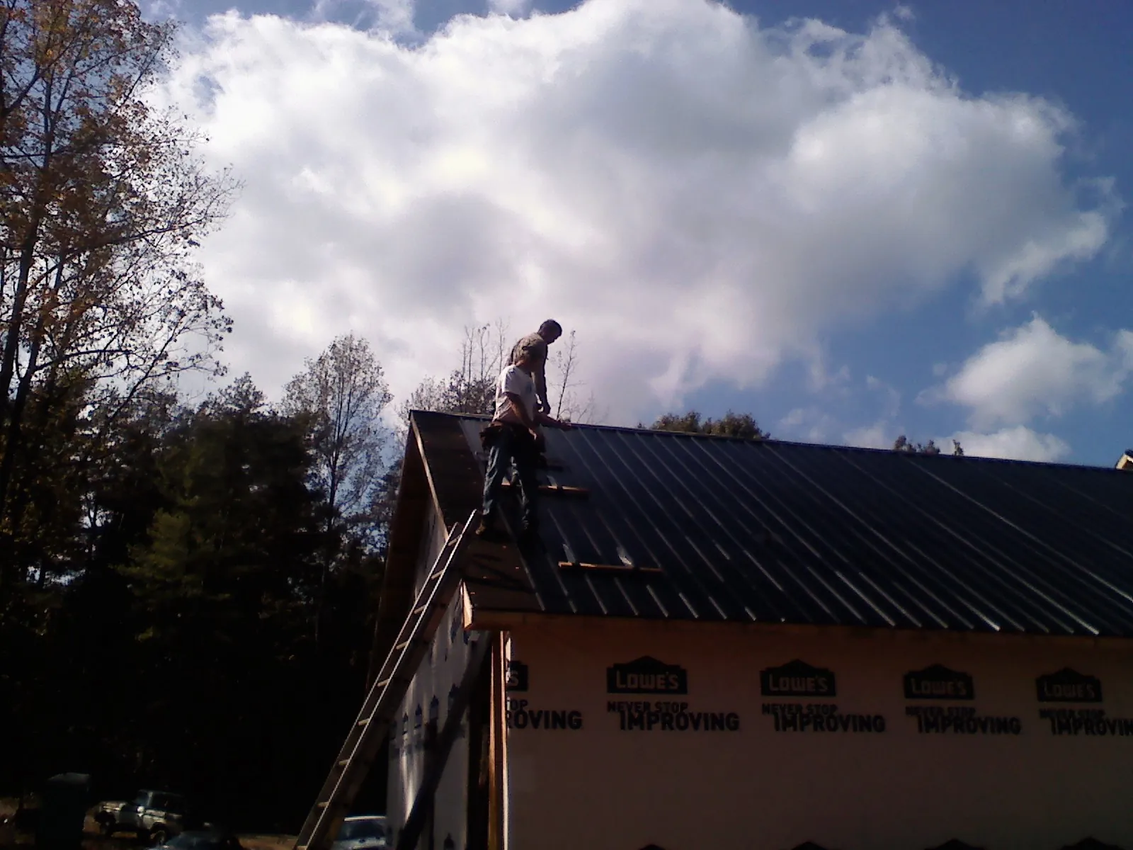 Roofer fastening dark metal panels high against a cloudy sky, from a Roof Inspection job in Saint Clair Shores
