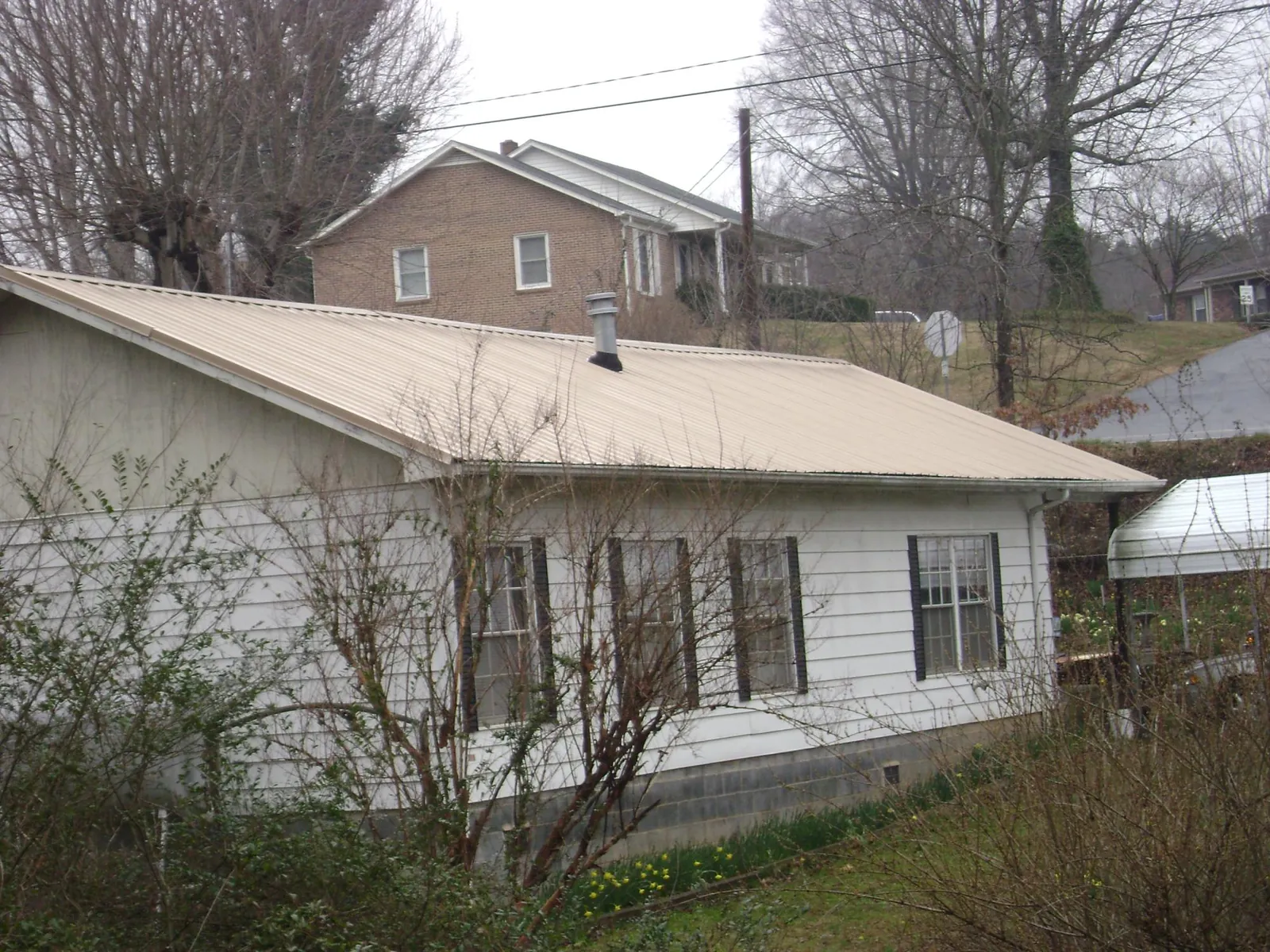 Tan metal roof on a white sided house set into a hillside — Commercial Roofing by Roofing Brothers in Saint Clair Shores